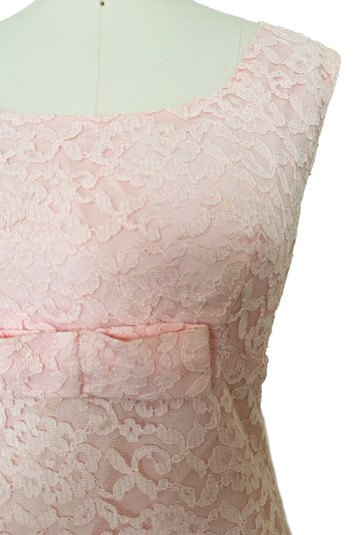 Detail view of 1960s vintage pink lace Mod empire waist cocktail shift dress, size medium to large. Showing the scoop neckline and bow at the waist.