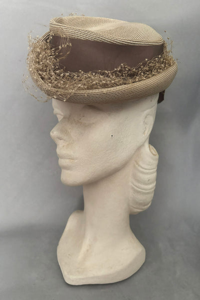 Vertical 3/4 view of 1940s vintage taupe straw riding style tilt topper hat with matching petersham ribbon and veiling trim, by Marche.