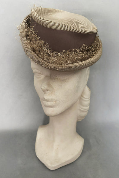 Vertical 3/4 view of 1940s vintage taupe straw riding style tilt topper hat with matching petersham ribbon and veiling trim, by Marche.