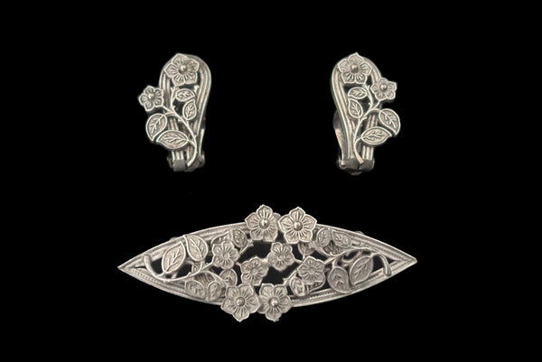 Horizontal front view of 1950s vintage Whiting and Davis pewter floral brooch and clip-on earrings jewelry set.