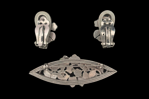 Horizontal back view of 1950s vintage Whiting and Davis pewter floral brooch and clip-on earrings jewelry set.