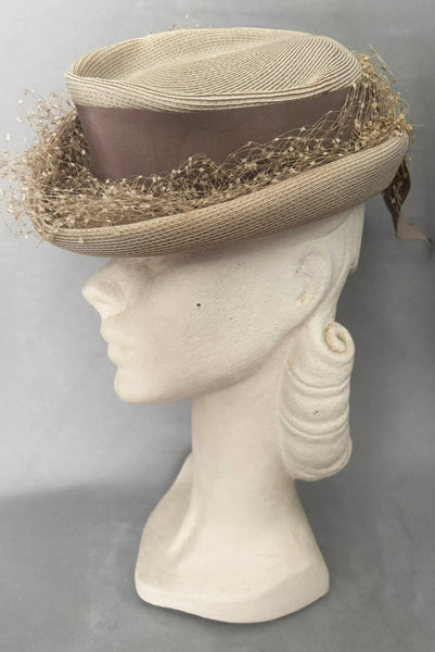 Vertical side view of 1940s vintage taupe straw riding style tilt topper hat with matching petersham ribbon and veiling trim, by Marche.