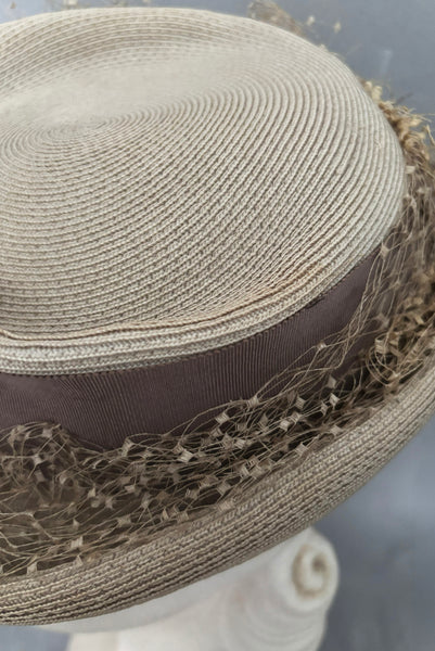 Detail view of 1940s vintage taupe straw riding style tilt topper hat with matching petersham ribbon and veiling trim, by Marche. Showing a light mark on the straw.