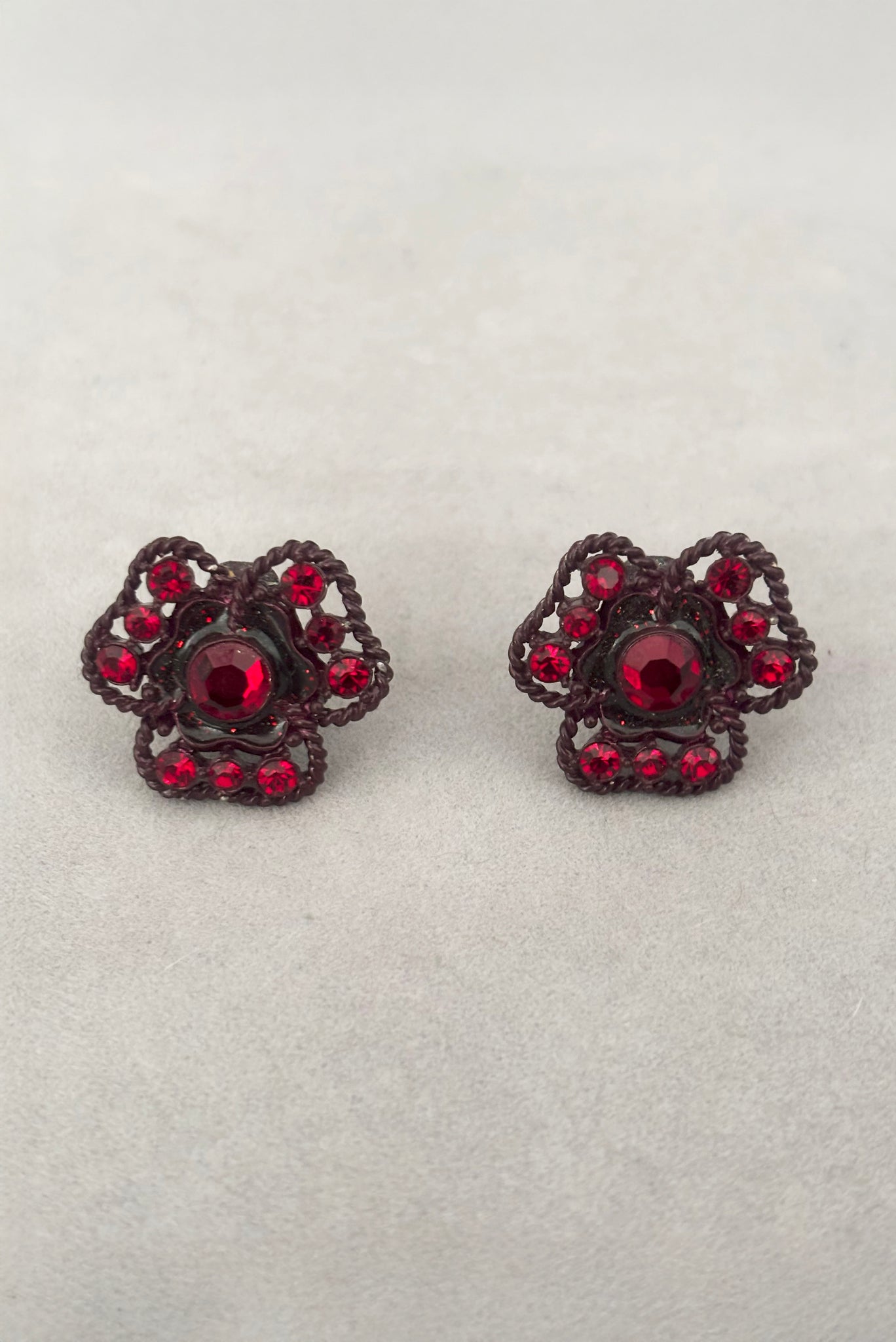 Vertical front view of 1960s vintage brown painted metal three leaf clover red rhinestone clip-on earrings.