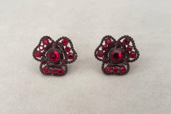 Horizontal front view of 1960s vintage brown painted metal three leaf clover red rhinestone clip-on earrings.