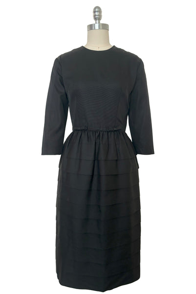 Front view of 1960s vintage crew neck, 3/4 sleeve, bow trimmed black faille cocktail dress, with tiered skirt, size small to medium.