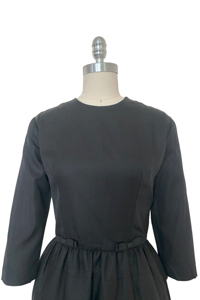 Bodice front view of 1960s vintage crew neck, 3/4 sleeve, bow trimmed black faille cocktail dress, with tiered skirt, size small to medium.