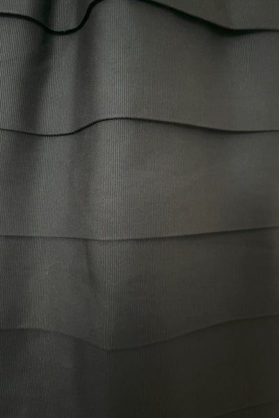 Detail view of 1960s vintage crew neck, 3/4 sleeve, bow trimmed black faille cocktail dress, with tiered skirt, size small to medium. Showing a close up of the tiers of the skirt and the ribbed fabric.