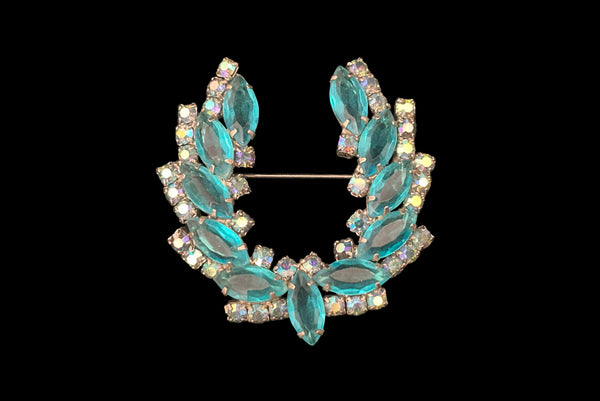 Horizontal front view 1950s vintage iridescent blue round  and aqua marquise rhinestone and silver tone metal horseshoe brooch.
