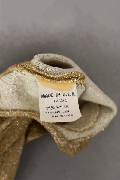 Interior detail view of 1950s vintage wrist length stretchy metallic gold nylon mylar gloves with clear rhinestone buttons. Showing the fabric composition tag.