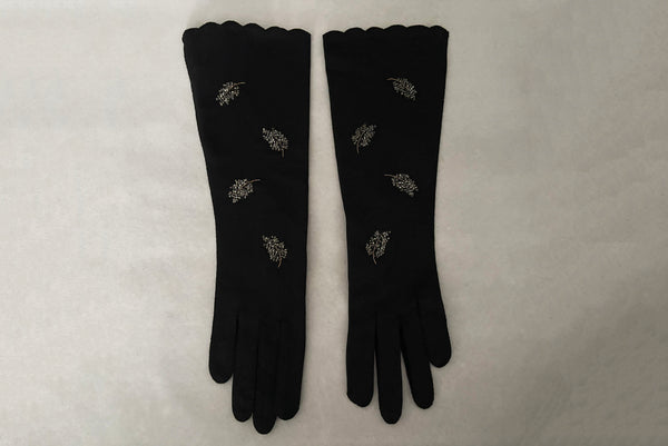 Horizontal front view of 1950s vintage mid length black Reindoe Nylon scalloped cuff gloves with gold embroidery and silver beaded leaves by Van Raalte, size 7.