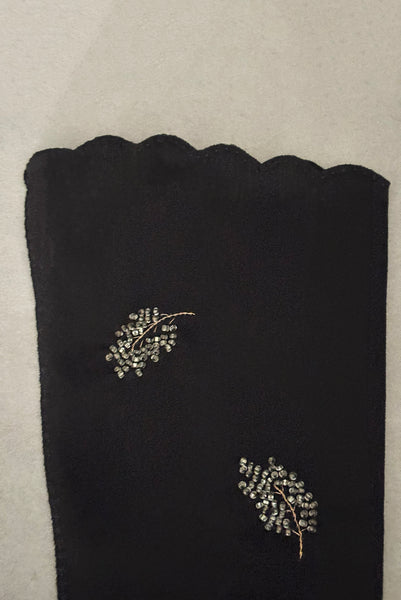 Detail view of 1950s vintage mid length black Reindoe Nylon scalloped cuff gloves with gold embroidery and silver beaded leaves by Van Raalte, size 7. Showing a close-up of the leaf embellishments and the scalloped cuff.