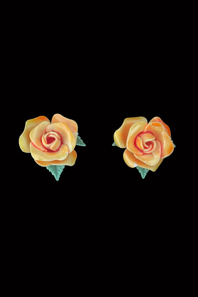 Vertical front view of 1950s vintage orange and green plastic rose clip-on floral earrings.