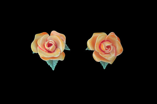 Horizontal front view of 1950s vintage orange and green plastic rose clip-on floral earrings.
