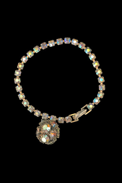 Vertical front view of 1950s vintage single line iridescent round rhinestone gold tone bracelet with matching rhinestone ball charm by Weiss.