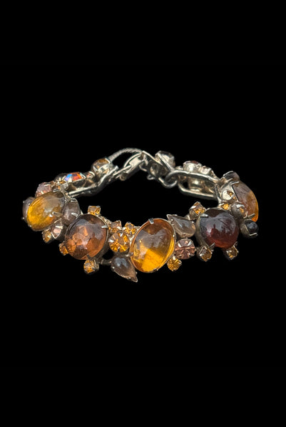 Vertical front view of 1950s vintage Weiss autumnal orange, brown, and iridescent rhinestone and foil backed glass cabochon gold tone bracelet.