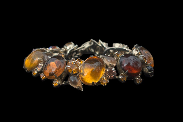 Horizontal front view of 1950s vintage Weiss autumnal orange, brown, and iridescent rhinestone and foil backed glass cabochon gold tone bracelet.