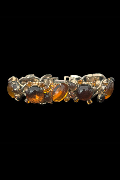 Vertical front view of 1950s vintage Weiss autumnal orange, brown, and iridescent rhinestone and foil backed glass cabochon gold tone bracelet.