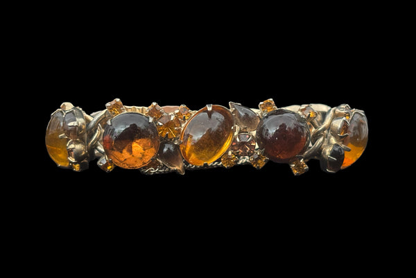Horizontal front view of 1950s vintage Weiss autumnal orange, brown, and iridescent rhinestone and foil backed glass cabochon gold tone bracelet.