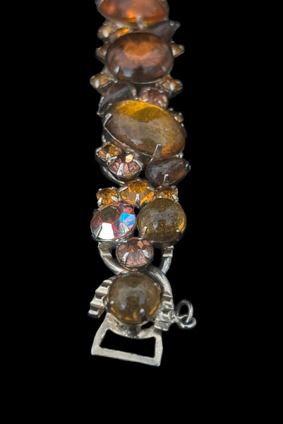 Detail view of 1950s vintage Weiss autumnal orange, brown, and iridescent rhinestone and foil backed glass cabochon gold tone bracelet. Showing some dark spots in the glass cabochons.