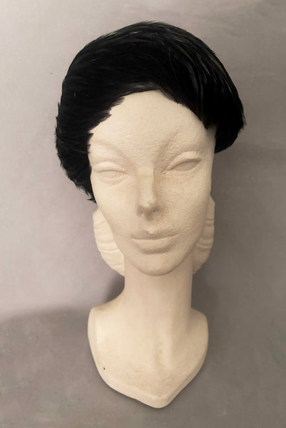 Vertical front view of 1960s vintage jet black feather and felt casque hat. On a mannequin head.