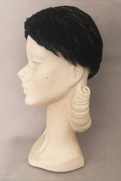 Vertical side view of 1960s vintage jet black feather and felt casque hat. On a mannequin head.