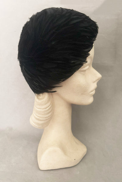 Vertical side view of 1960s vintage jet black feather and felt casque hat. On a mannequin head.