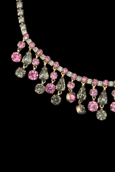 Detail front view of 1950s vintage pink & gray round and pear cut rhinestone gold tone necklace and earrings demi-parure jewelry set. Showing a close-up of the necklace center front with pear and round rhinestone drops.