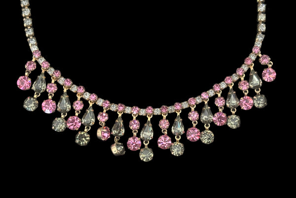 Detail front view of 1950s vintage pink & gray round and pear cut rhinestone gold tone necklace and earrings demi-parure jewelry set. Showing a close-up of the necklace center front with pear and round rhinestone drops.