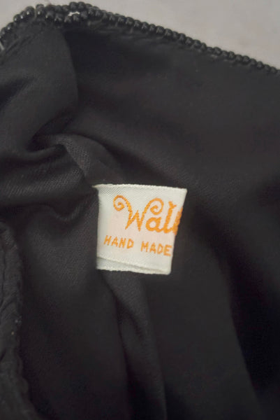 Interior detail view of 1960s vintage black satin floral beaded fold over clutch evening bag by Walborg. Showing a close up of the black glass seed beads worked into a flower pattern. Showing one side of the Walborg label.