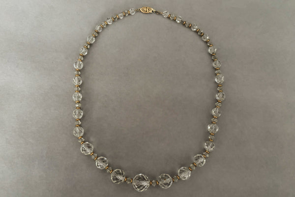 Horizontal view of 1960s vintage graduated clear crystal bead necklace with gold tone spacers.