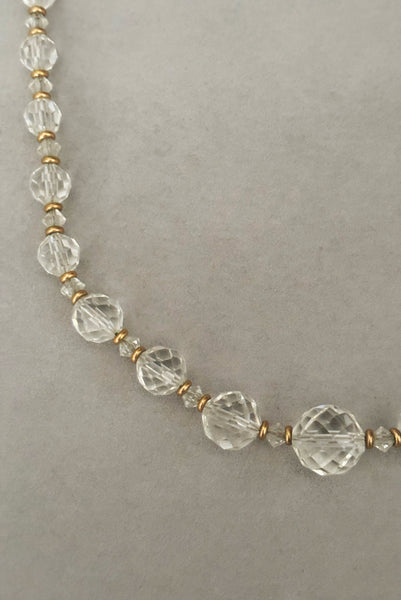 Detail view of 1960s vintage graduated clear crystal bead necklace with gold tone spacers. Showing a close-up of the round and bicone beads with gold disk spacers.
