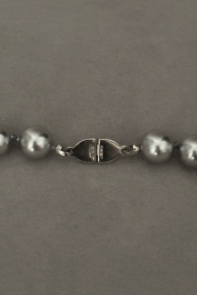 Detail view of 1980s vintage designer gray faux pearl bead necklace, by Monet. Showing a close-up of the back of the silver tone clasp with the Monet stamp.