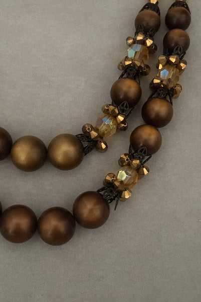 Detail view of 1950s vintage brown and yellow double strand beaded necklace and clip-on earrings demi parure set by Hobé. Showing a close-up of the brown satin finish beads, yellow faceted crystal beads, gold bicone crystal beads, and black metal filigree caps on the necklace.