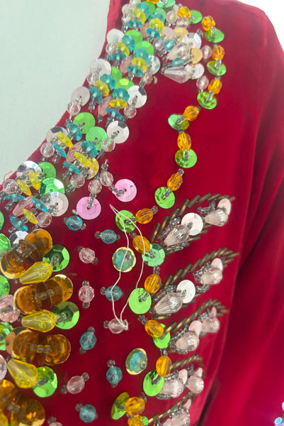 Front detail view of 1960s vintage Mardi Gras costume red velvet beaded caftan/dress, small to medium. Showing the pink, green, blue, yellow, and clear sequins, plastic beads, and glass beads. With an area of minor bead loss.