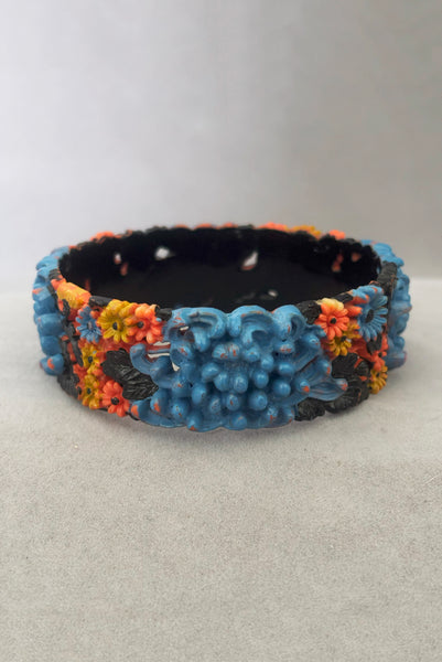 Vertical front view of 1930s vintage blue, black, and yellow painted and floral carved coral mum celluloid bangle bracelet.