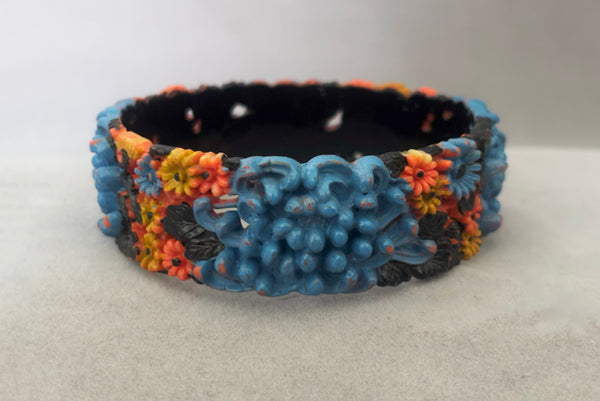 Horizontal front view of 1930s vintage blue, black, and yellow painted and floral carved coral mum celluloid bangle bracelet.