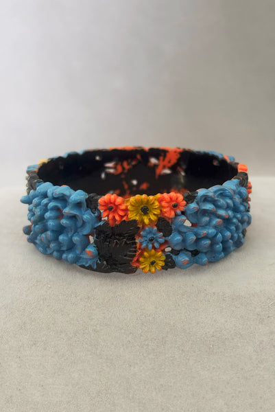 Vertical back view of 1930s vintage blue, black, and yellow painted and floral carved coral mum celluloid bangle bracelet.