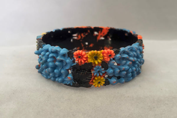 Horizontal back view of 1930s vintage blue, black, and yellow painted and floral carved coral mum celluloid bangle bracelet.