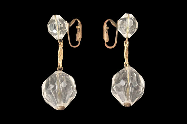 Horizontal side view of 1960s vintage mod clear faceted Lucite bead and gold tone metal top and drop clip-on earrings.