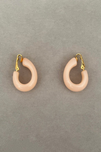 Vertical side view of 1980s vintage pink Lucite plastic and gold tone clip-on hoop earrings by Crown Trifari.