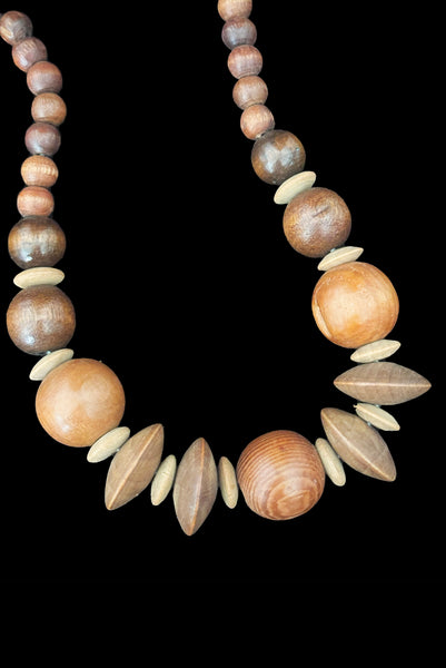 Detail view of 1980s vintage carved round and disk bead light, medium, and dark triple tone wood necklace. Showing some irregularities in the carving on the right large round medium wood bead.
