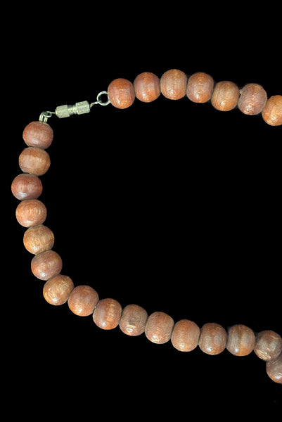 Detail view of 1980s vintage carved round and disk bead light, medium, and dark triple tone wood necklace. Showing a close-up of the silver tone barrel clasp.