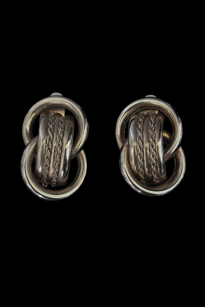 Vertical front view of 1980s vintage gold tone interlocking hollow tube rope chain trimmed clip-on statement earrings.