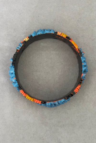 Vertical top view of 1930s vintage blue, black, and yellow painted and floral carved coral mum celluloid bangle bracelet.