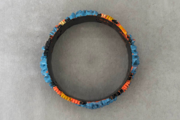 Horizontal top view of 1930s vintage blue, black, and yellow painted and floral carved coral mum celluloid bangle bracelet.