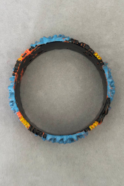 Vertical bottom view of 1930s vintage blue, black, and yellow painted and floral carved coral mum celluloid bangle bracelet.