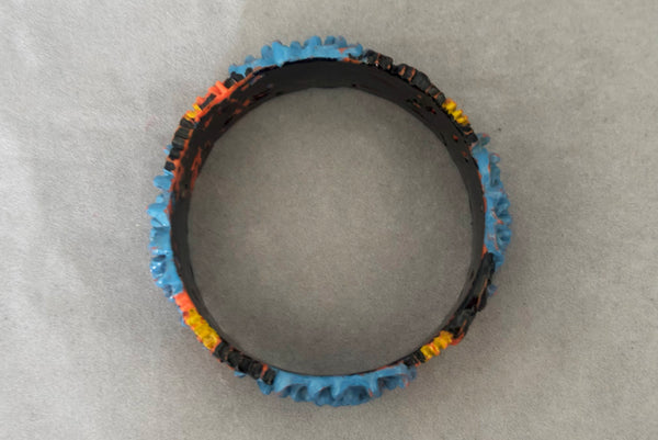 Horizontal bottom view of 1930s vintage blue, black, and yellow painted and floral carved coral mum celluloid bangle bracelet.
