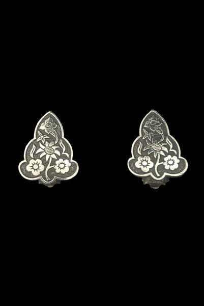 Horizontal perspective view of 1960s vintage silver tone and black floral scalloped triangular clip-on earrings for unpierced ears.