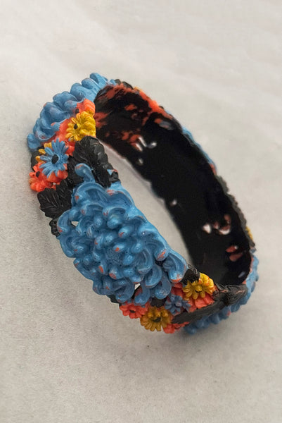 Vertical perspective view of 1930s vintage blue, black, and yellow painted and floral carved coral mum celluloid bangle bracelet.